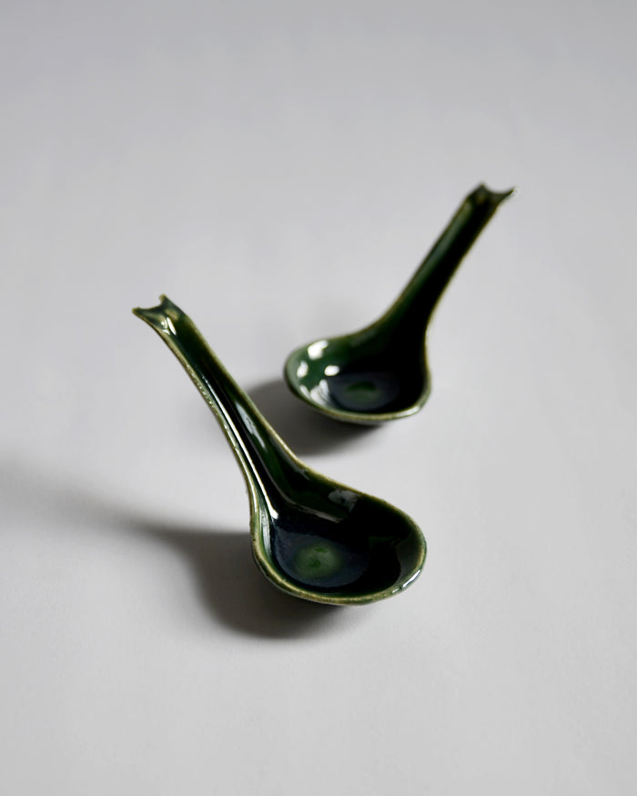 Front view of 2 staggered oribe green Ceramic Soup Spoons by Azmaya against white-gray background.