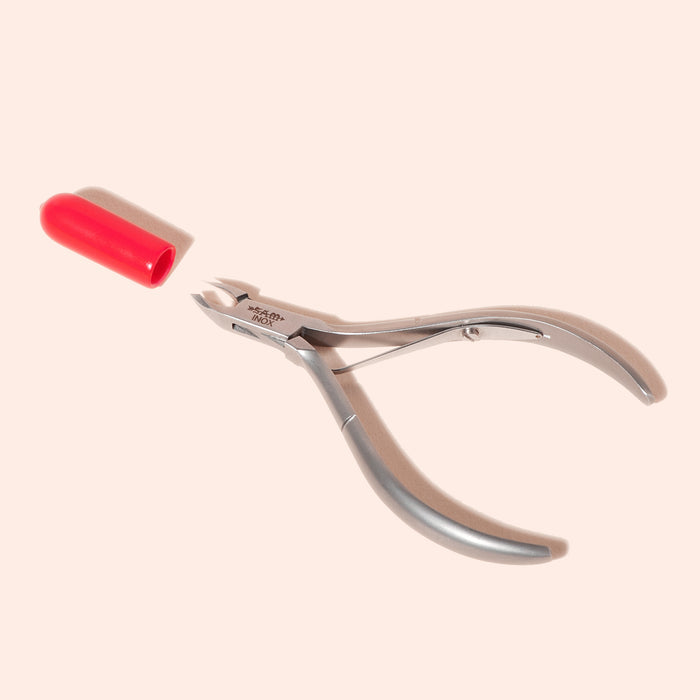 Manucurist Cuticle Clippers—professional stainless steel tool with a curved handle and separate red cap, shown on a light beige background—for neat, precise trimming.