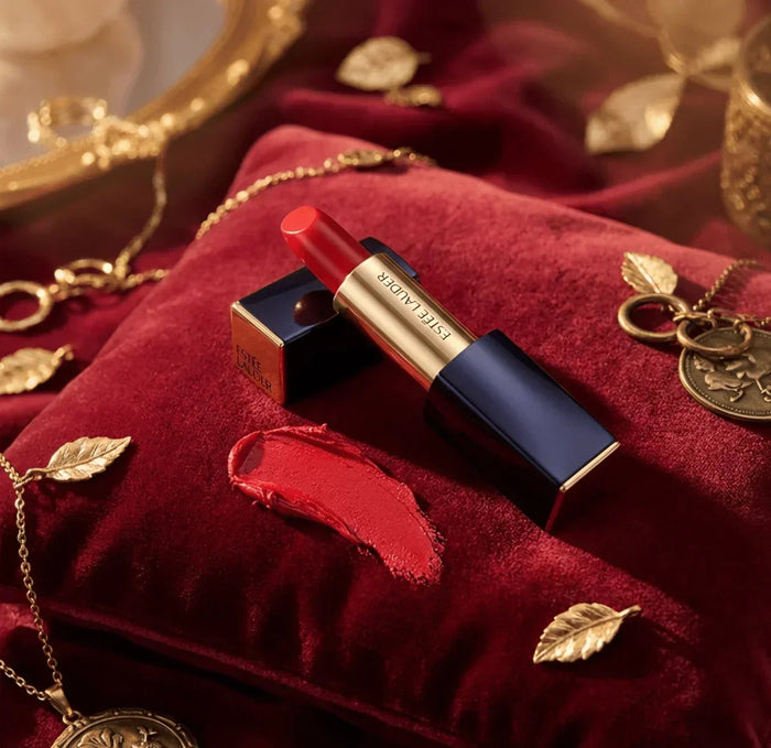 Red lipstick on a velvet cushion with gold jewelry and lipstick swatch nearby