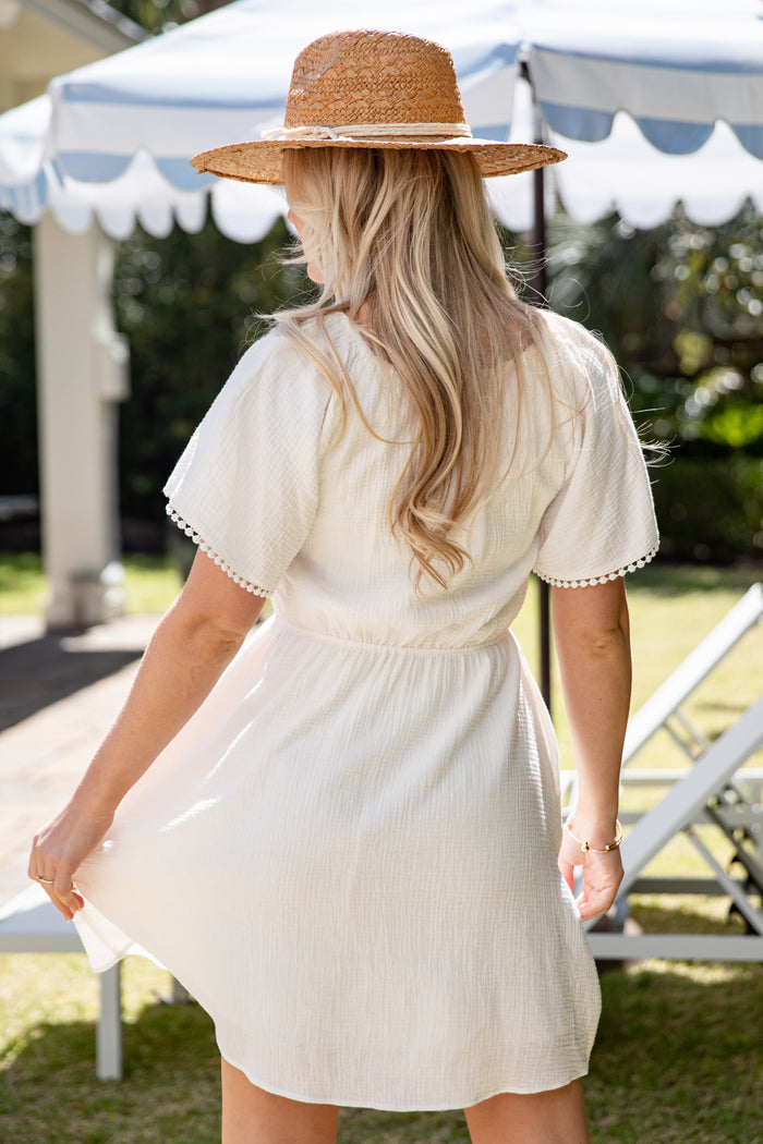 Woman in a white dress and straw hat standing outdoors under a tent.