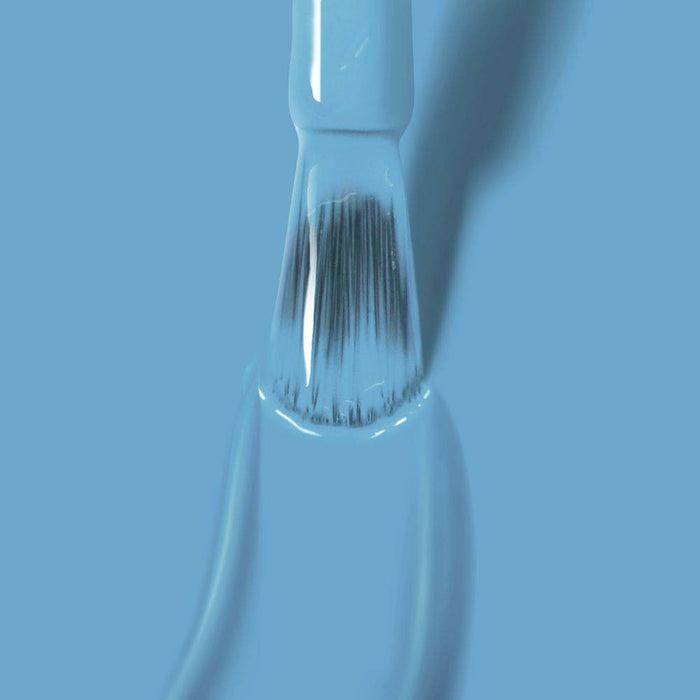 A close-up of a paintbrush coated in Hot Spring by LONDONTOWN against a serene blue background.