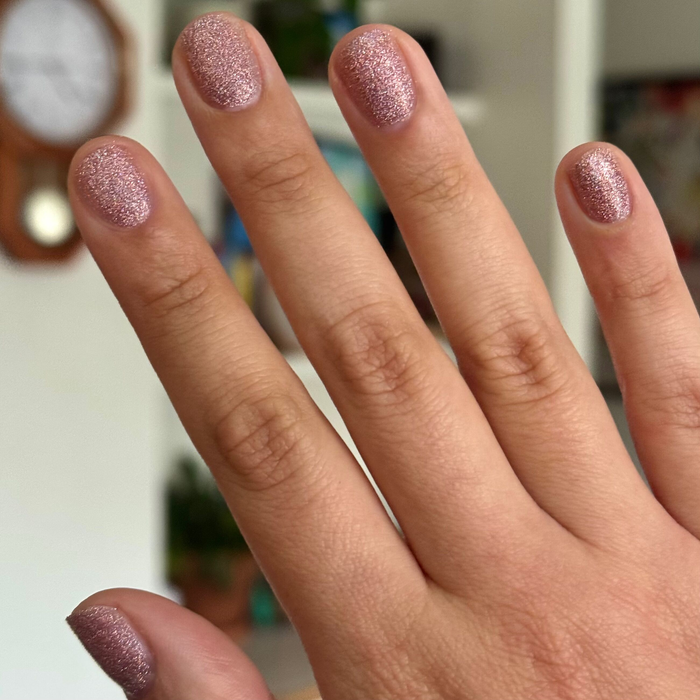 Hand showing nails painted with MWAH packed pink holographic glitter quick dry polish by Olive and June