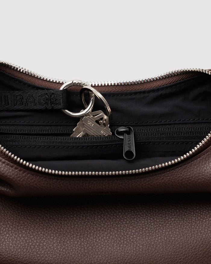 Close-up of zip-top hardware, metal ring and lock on brown recycled leather crescent bag