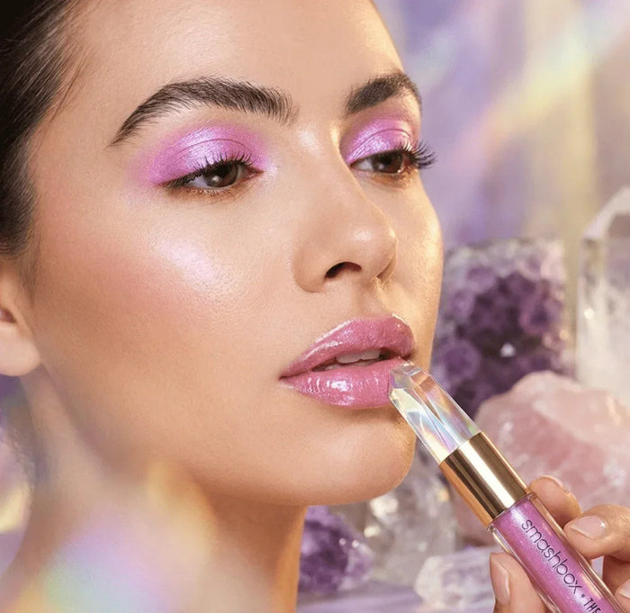 Woman applying iridescent shimmer lipstick with matching pink shimmer eyeshadow