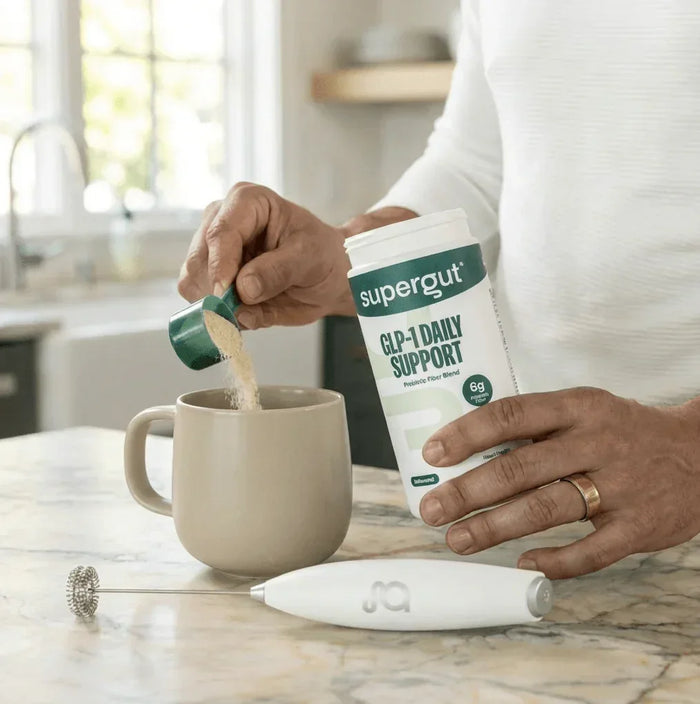 Person adding Supergut GLP-1 Daily Support prebiotic fiber powder to mug on kitchen counter