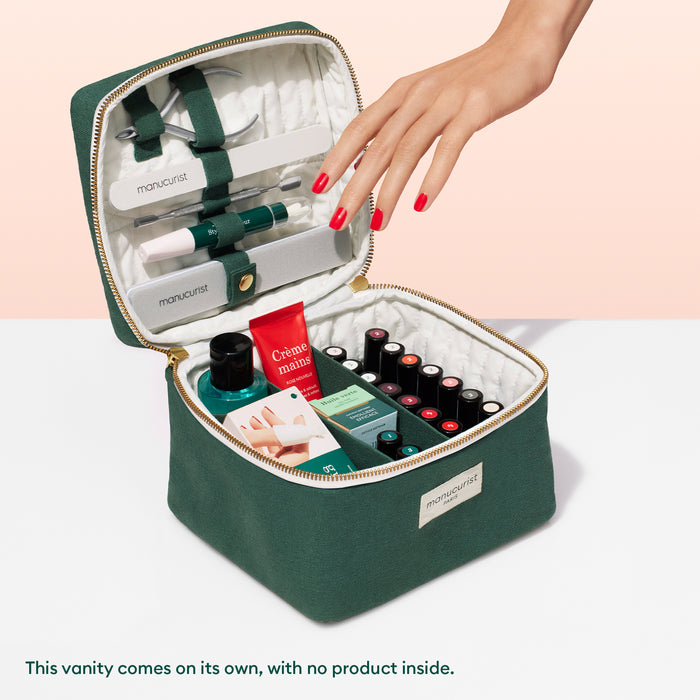 A hand with red-painted nails reaches into a Manucurist-test Vanity Case, neatly organized with elastic straps and compartments, and filled with manicure essentials like nail polishes, hand cream, and tools.