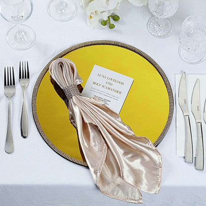 Elegant gold charger plate with a silk napkin and wedding invitation on a dining table.