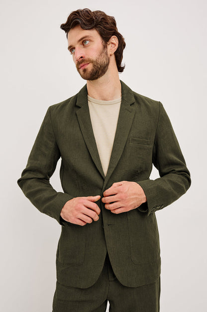 The Bond is a single breasted blazer with two buttons, one chest pocket and two patch pockets in Deep Olive colorway. Front view featured on model.