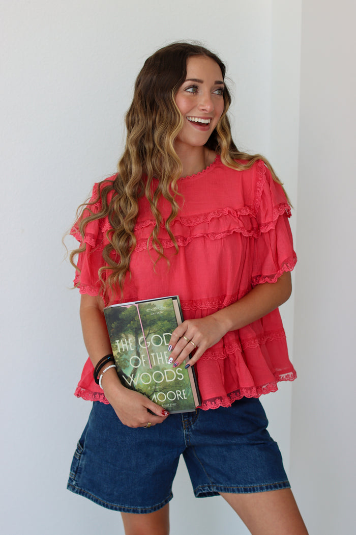 Woman wearing a coral ruffled top against a white background