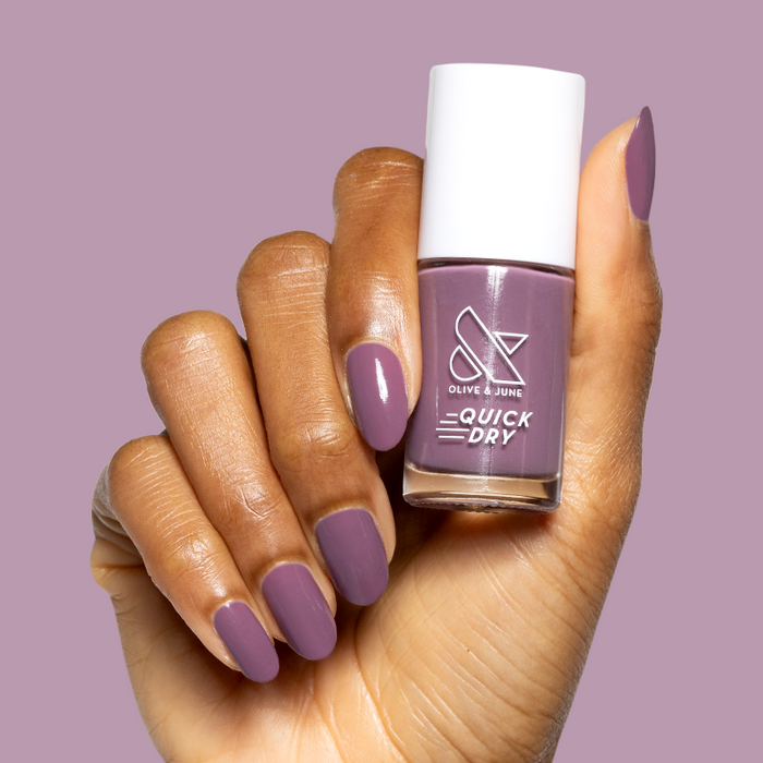 Hand holding Cardigan quick dry gel polish bottle showing matching mauve manicure on medium-length nails on mauve background