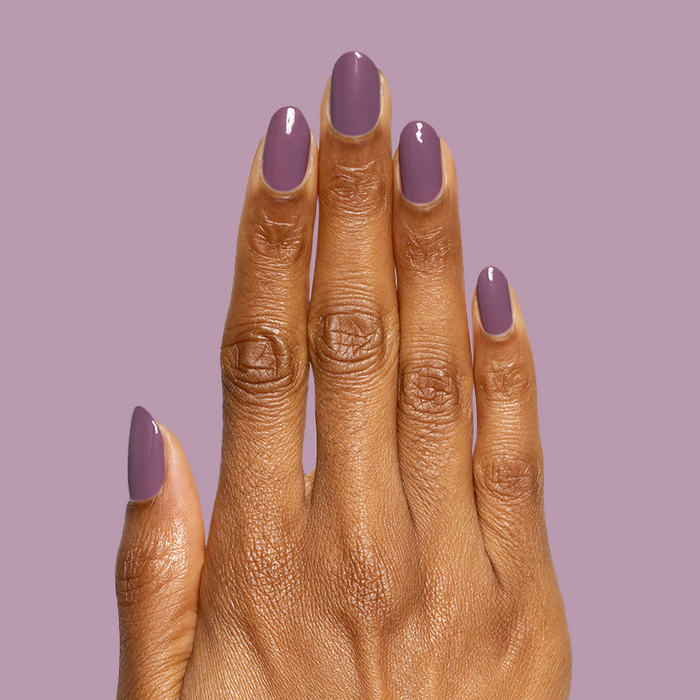 Hand with glossy Cardigan gel polish manicure in warm mauve shade on medium-length nails against mauve background