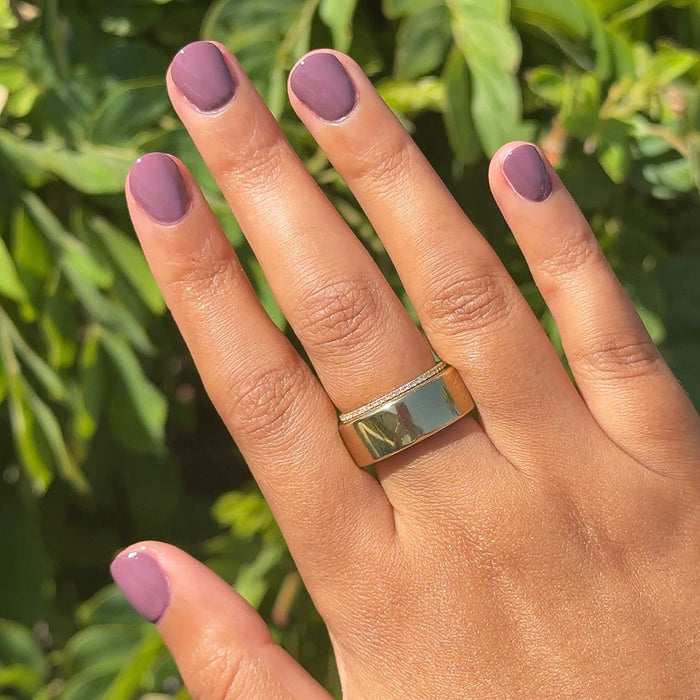 Hand with glossy Cardigan gel polish manicure in true mauve shade on short nails against green foliage background