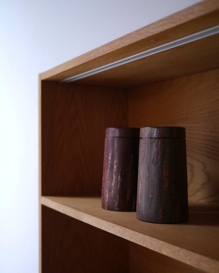Two wooden cylindrical coffee container by Denshiro on a wooden shelf with a white background