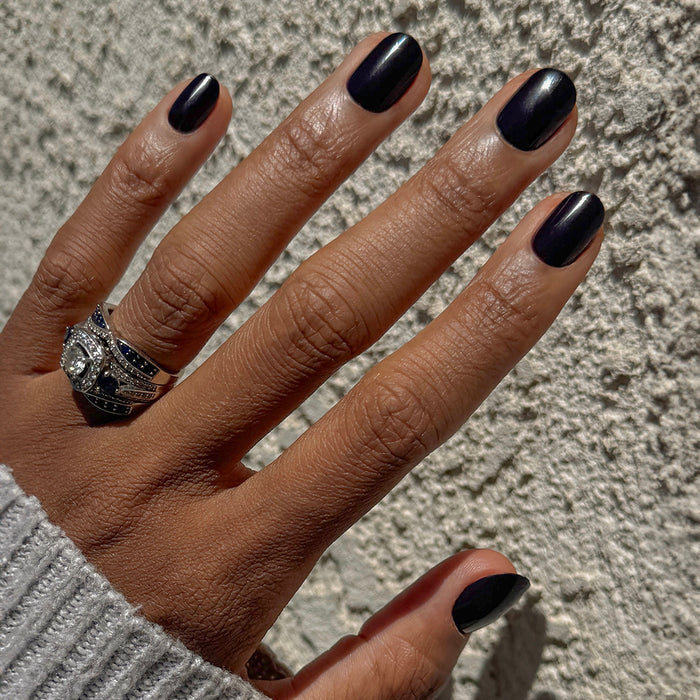 Covet | Extra Short | Round - Tab Press-On nails in rich dark plum shade on hand with rings against textured background