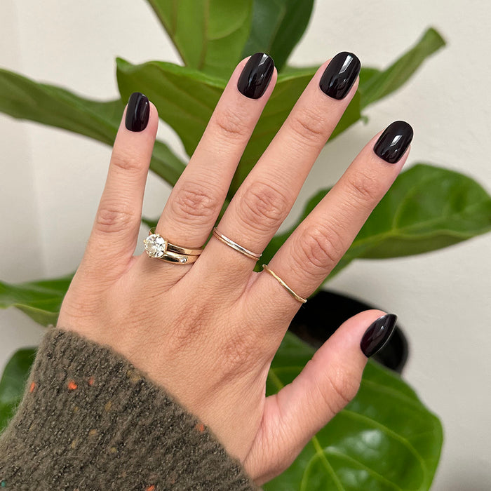 Covet | Extra Short | Round - Tab Press-On nails in deep dark plum shade with glossy finish on hand with rings over green leaves background
