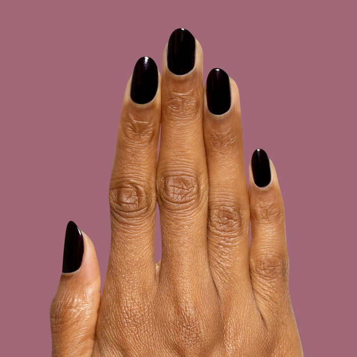 Hand with deep dark plum Covet gel polish manicure on medium-length natural nails against muted plum background