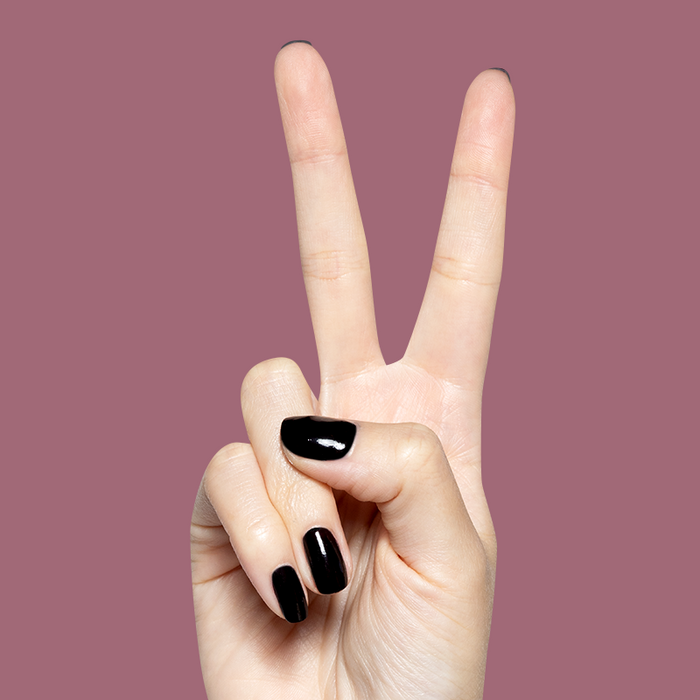 Hand showing peace sign with glossy dark plum Covet gel polish manicure on short natural nails against muted mauve backdrop