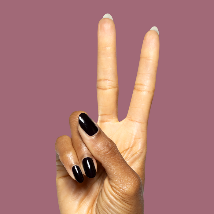 Hand showing peace sign with glossy deep plum Covet gel polish manicure on natural nails against muted mauve backdrop