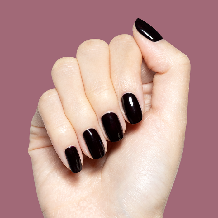 Hand with glossy deep plum Covet gel polish manicure on medium-length natural nails against muted plum background