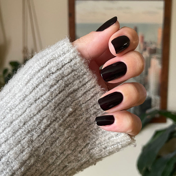 Hand with glossy Covet gel polish manicure in dark plum shade on medium-length nails wearing cozy knit sweater sleeve