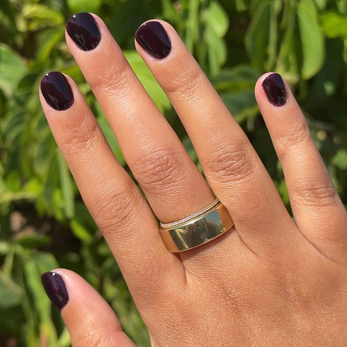 Hand with glossy deep plum Covet gel polish manicure on short natural nails against green outdoor background