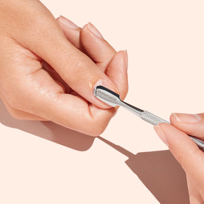 A hand uses the Manucurist Cuticle Pusher to gently push back a fingernail cuticle, showcasing precise nail care against a pale background.