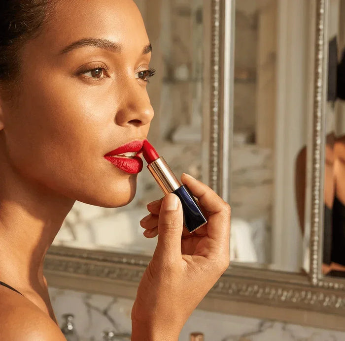 Woman applying red lipstick in front of bathroom mirror, close-up beauty shot
