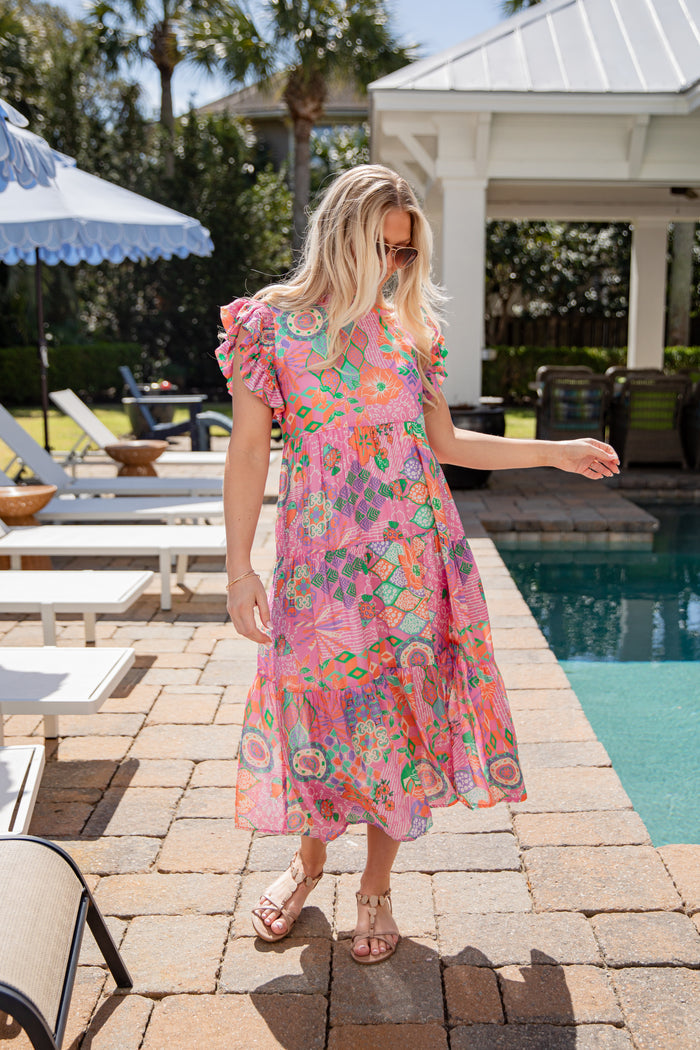 Woman in a colorful dress standing by a poolside with lounge chairs and umbrellas.
