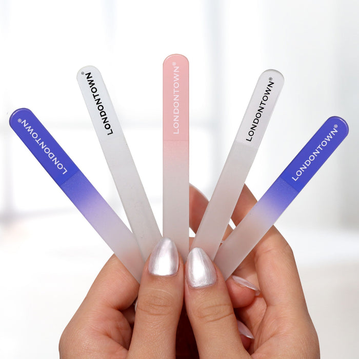 A hand with silver nail polish holds a set of five Glass Nail Files - Petal by LONDONTOWN, featuring shades from blue to pink and promising effortless, damage-free nail filing.