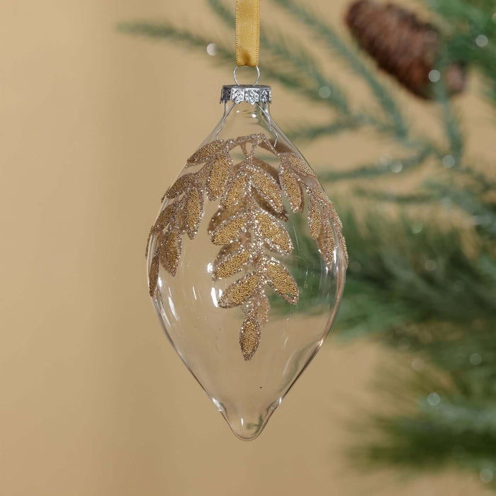 Clear glass ornament with gold leaf design hanging on a tree.