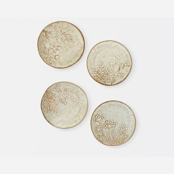 Four round ceramic coasters with embossed botanical designs in a warm beige and cream glaze, arranged on a light gray background.
