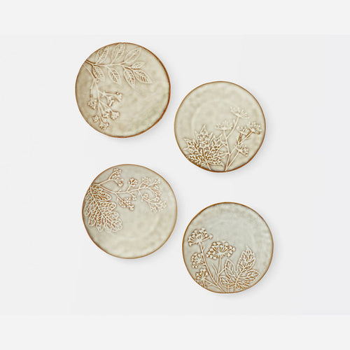 Four round ceramic coasters with embossed botanical designs in a warm beige and cream glaze, arranged on a light gray background.