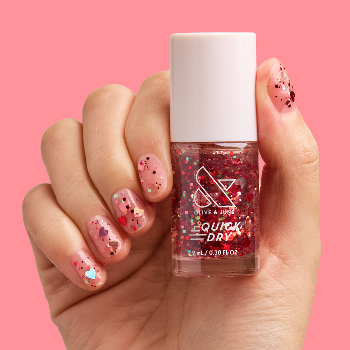 Hand holding bottle of HEARTED quick dry polish with nails decorated in heart-shaped confetti manicure