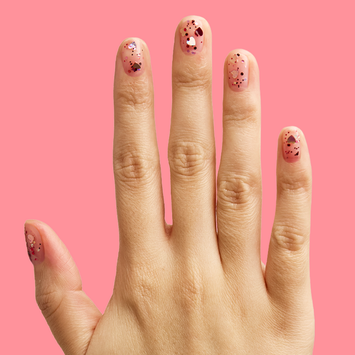 Hand displaying manicure with HEARTED quick dry polish featuring heart and sequin confetti on pink background