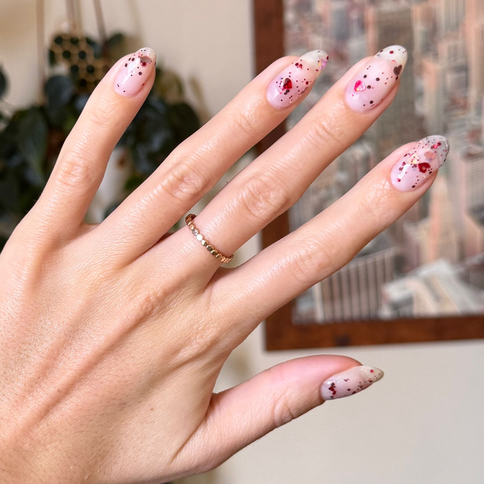 Hand with manicure featuring HEARTED quick dry polish topped with heart and sequin confetti on natural nails