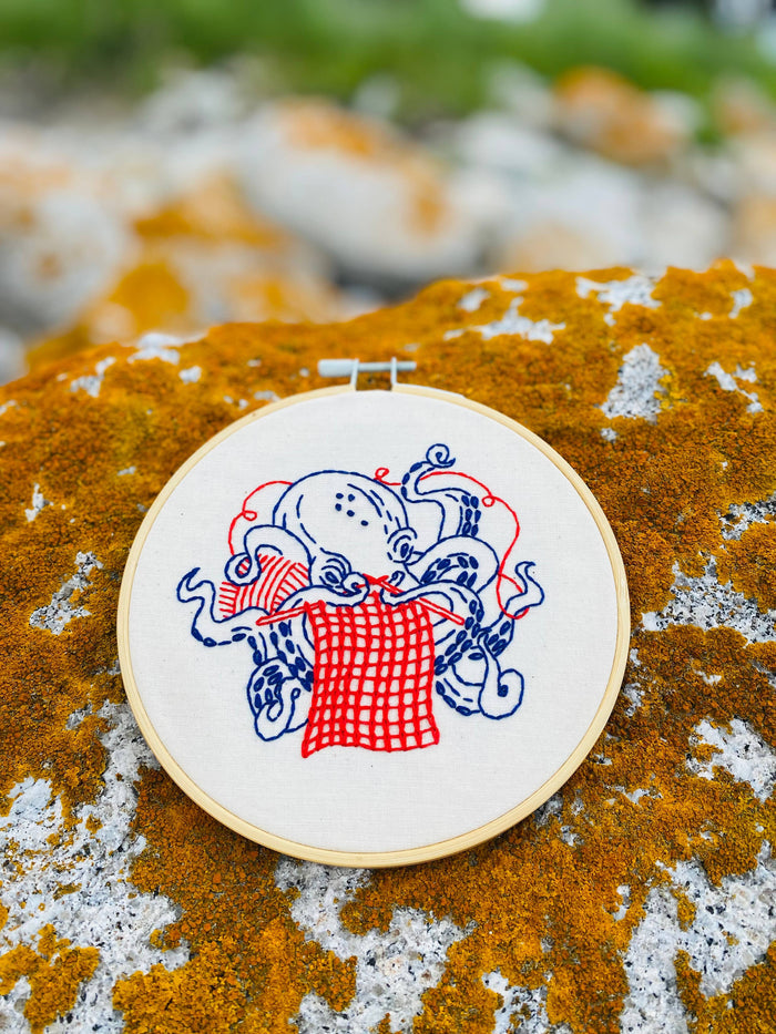 Embroidery hoop with a design of an knitting octopus on a textured rock surface.