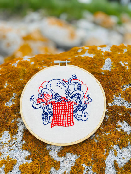 Embroidery hoop with a design of an knitting octopus on a textured rock surface.