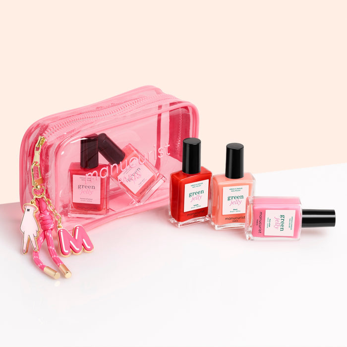 Three bottles of pink, orange, and clear nail polish stand before the Manucurist Jelly Summer Pouch—a transparent bag with a tassel-and-charm keychain—perfect for on-the-go manicures.