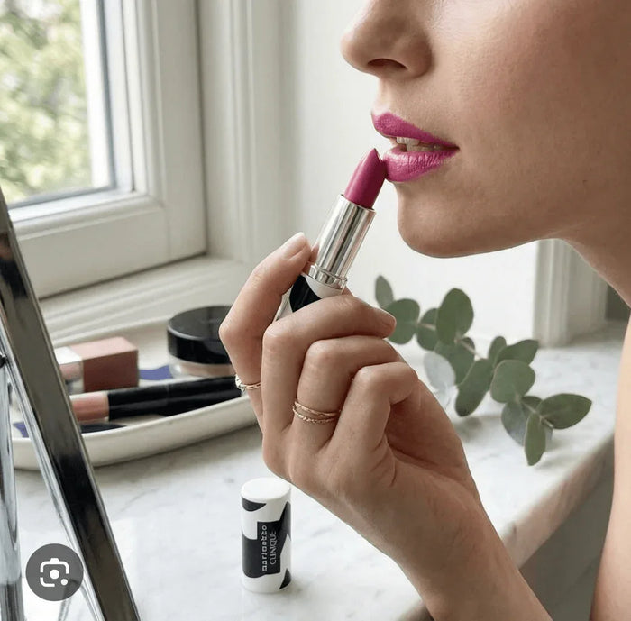 Woman applying pink lipstick with silver tube near window, close-up, beauty makeup routine