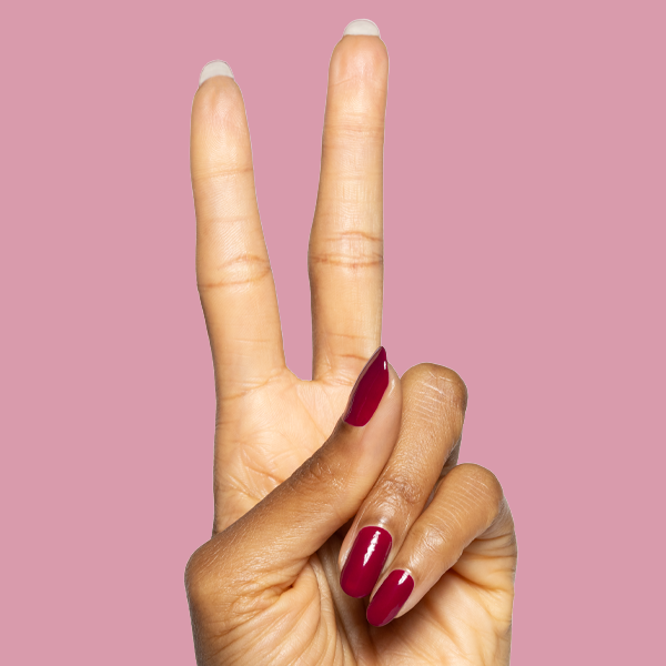 Hand showing peace sign with glossy Mulberry deep maroon gel polish manicure on natural nails against light pink background