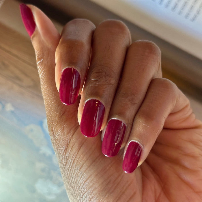 Hand with polished nails featuring glossy Mulberry gel polish in deep maroon shade indoors against blurred background