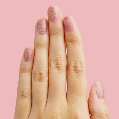 Hand with nails painted in glittery pink holographic MWAH quick dry polish by Olive and June on pink background