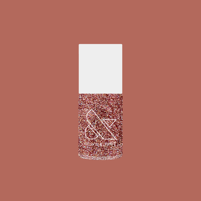Bottle of MWAH quick dry polish with packed pink holographic glitter by Olive and June on muted rose background