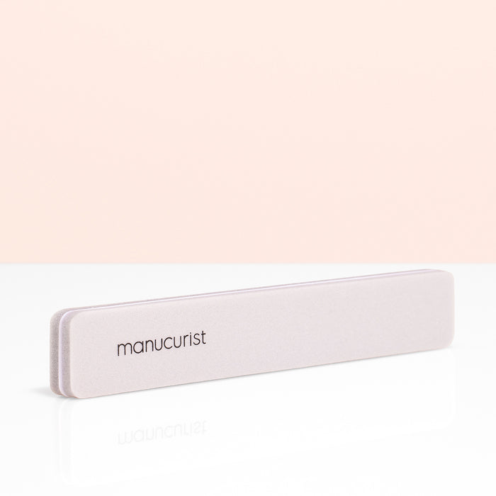 A light pink Manucurist Nail Buffer Sponge, ideal for manicure prep, is shown on a white surface with a pale peach background.