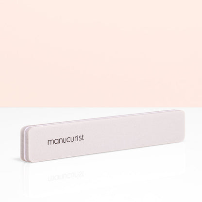 A light pink Manucurist Nail Buffer Sponge, ideal for manicure prep, is shown on a white surface with a pale peach background.