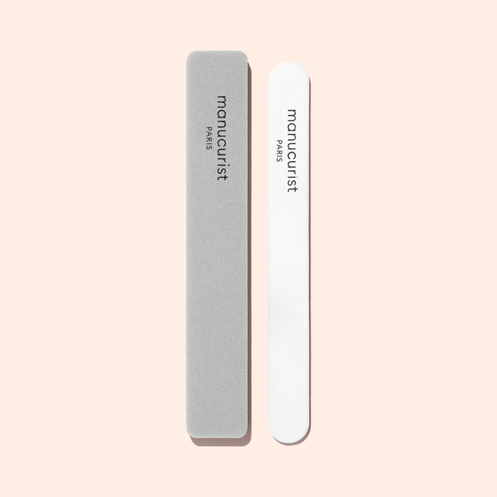 A Manucurist Nail Buffer Sponge with rounded edges sits next to a gray nail file, both ready to smooth your nails on a light beige background.
