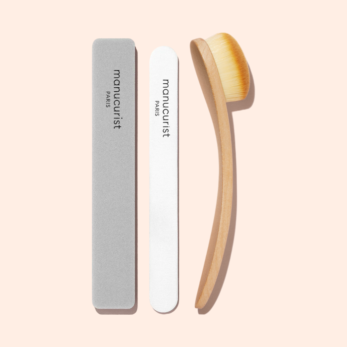 Three manicure tools on a light pink background: a gray nail file, the Manucurist Nail Buffer Sponge for smoothing nails, and a wooden-handled brush with dense bristles, all branded Manucurist.