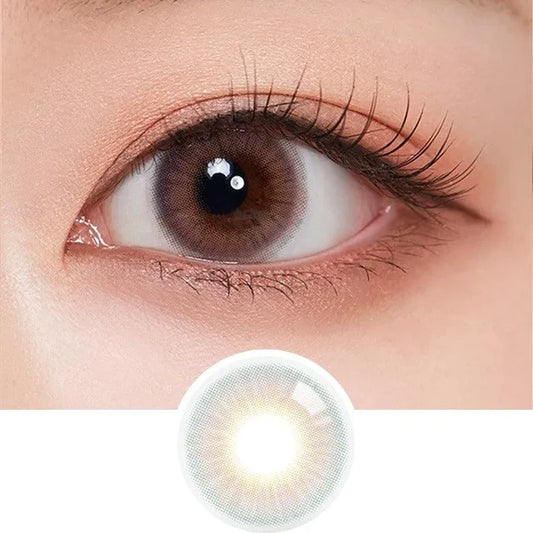 A close-up of a brown eye with long lashes wearing Olola Blow Sunset Pink contact lenses by Olola for a natural look. Below, an enlarged image of the lens is shown; suitable for those needing myopia prescription.