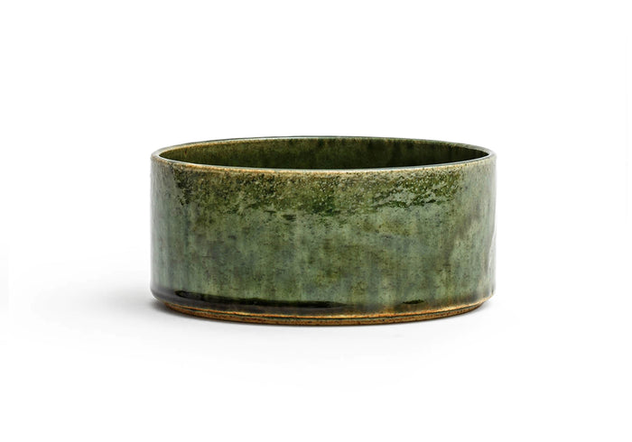 Silhouetted image of small ceramic oribe bowl with deep green glaze by Time and Style against white background.