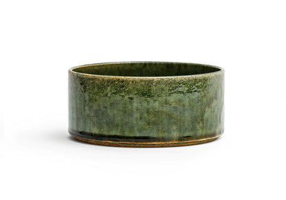 Silhouetted image of small ceramic oribe bowl with deep green glaze by Time and Style against white background.